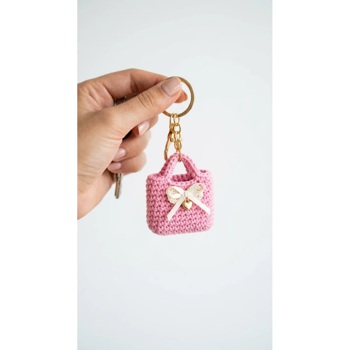 Pink gift bag crochet keychain with white lace bow and golden heart charm held in hand