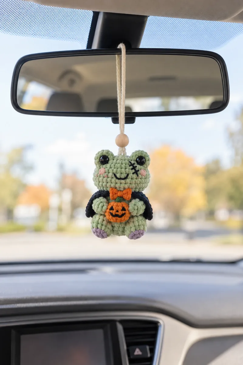 AI concept of a sage-green crochet frog with an orange bow, pumpkin and dark cape